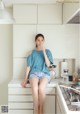 A woman sitting on a kitchen counter drinking a glass of water.