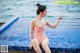 A woman in a pink bathing suit sitting on the edge of a swimming pool.