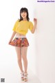 A woman in a yellow shirt and a colorful skirt posing for a picture.