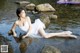 A woman in a white dress sitting on a rock in the water.