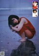 A woman in a red dress crouching on the beach.