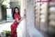 A woman in a red dress leaning against a wall.